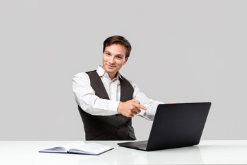 Successful man in a white t-shirt and grey vest is pointing at the screen of a laptop.