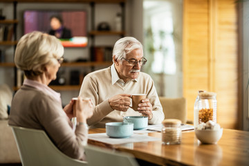 Senior man reading newspaper while drinking coffee with his wife in the morning.