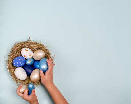 Children's hands lay blue Easter eggs in a nest with eggs on a blue background with place for copy space