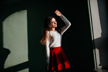 Obraz na płótnie Canvas Romantic brown-haired lady enjoying sunlight while posing in the dark. Indoor photo of graceful white woman in trendy red skirt standing in shadow with smile.