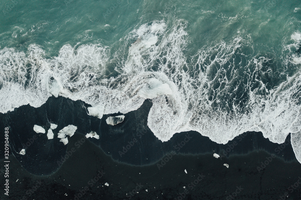 Wall mural crashing waves on a volcanic black sand beach with ice from above