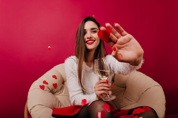 Glad dark-haired woman enjoying tasty champagne during date. Ecstatic female model in white sweater...