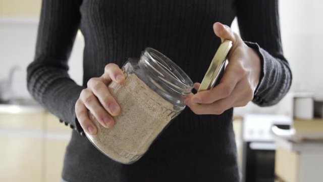 Medium shot as opening a jar full with gluten-free brown wheat. Kitchen preparation concept.