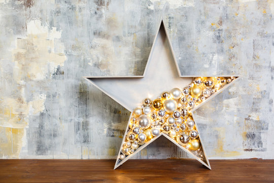 Wooden star with lamps and garland near gray plaster wall in studio