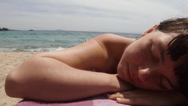 Close up of a girl sunbathing on a beach in Greece. Careless lying with hew eyes closed.