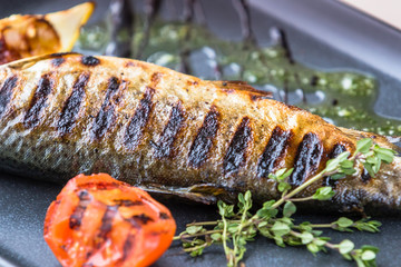 River trout grilled with tomato and lemon on a rectangular plate. Decorated with marjoram and sous