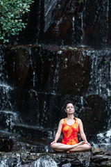 young girl doing yoga in the wild inside a waterfall of water
