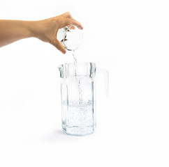 Hand pours water from a glass cup into a jug, isolated on white background