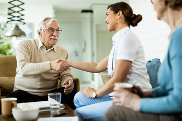 Fototapeta premium Happy senior man and female doctor handshaking during home visit.