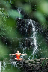 young girl doing yoga in the wild inside a waterfall of water - 320910345