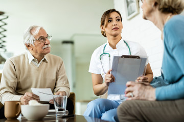 Below view of young healthcare worker talking to mature couple at home.