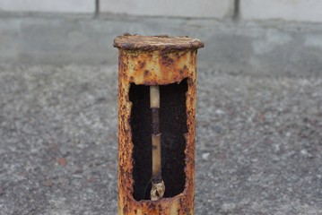 old iron pole in brown rust with a hole and an electric cable inside on the street on a gray background