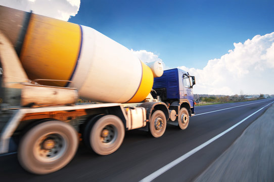 Concrete mixer truck on a countryside road in motion against a sky with clouds