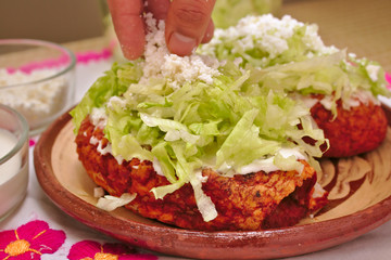 A side view of a traditional mexican food pambazo with lettuce, white cheese, cream and hot sauce