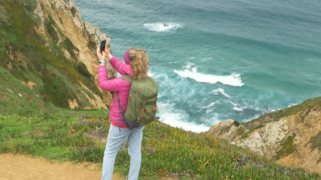 woman with large backpack takes picture from ocean coast