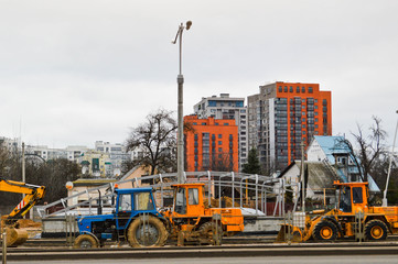 Many powerful industrial heavy specialized construction equipment of tractor excavators and bulldozers make road repairs during the construction of a new micro-district in a big city