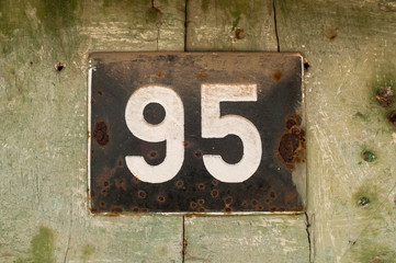 Weathered grunge square metal enameled plate of number of street address with number 95 closeup