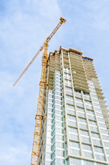 High-rise building under construction. The site with cranes against blue sky and white clouds