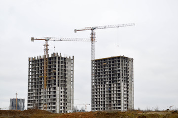Fototapeta na wymiar Construction of a new microdistrict with high houses, new buildings with developed infrastructure with the help of large industrial cranes and professional construction equipment in a big city