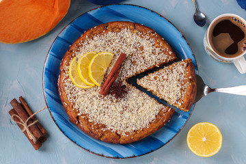 Homemade pumpkin pie with lemon, cinnamon and walnuts, sprinkled with coconut, sliced, on a light blue background, Top view