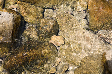 Stones in clear water, sun reflection, summertime. Natural background, top view, close up