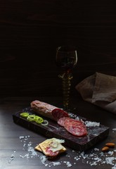 Smoked sausage with slices and crackers and a glass of red wine on a dark background