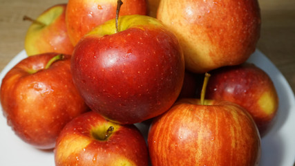 Ripe bright red Florina apples on a white ceramic plate on a wooden table