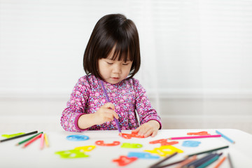toddler girl practice writing letters on white paper against white background