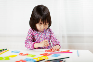 toddler girl practice writing letters on white paper against white background