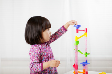 toddler girl play marble run game at gome agianst white background