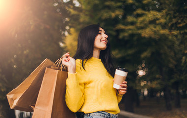 Woman in city park after mall shopping with bags, smartphone and cup fo coffee