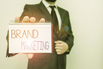 Conceptual hand writing showing Brand Marketing. Concept meaning creating a name that identifies and differentiates a product Male human wear formal work suit with office look hold book