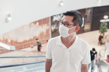 Middle aged Asian man wearing glasses and medical face mask in shopping mall, social distance, coronavirus, covid-19 virus outbreak, air pollution and health concept