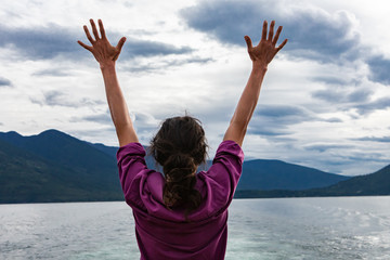 Close up from behind of a man on the deck of a passenger ferryboat. Arms raised and hands with fingers spread open. Freedom concept.