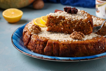 Homemade pumpkin pie with lemon, cinnamon and walnuts, sprinkled with coconut, sliced, on a light blue background with a cup of coffee