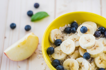 Morning breakfast with fruit pieces and blueberries all on a light wooden table.