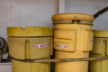 Two bright yellow plastic bins, labeled with oil Boom and Spill kit secured on the deck of a canadian ferry boat. Looking old and dirty.