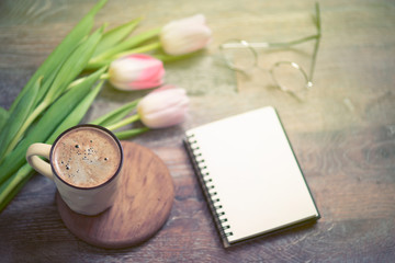 Obraz na płótnie Canvas Overhead shot a bouquet of an open book or garden planner, glasses, coffee, sissors and flowers over a wood table top ready to plan an agenda. Flat lay top view style.