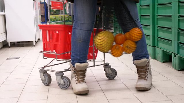 New environmentally friendly packaging for supermarket products. Mesh knitted from natural cotton threads. Adult girl put oranges in net and waving it next to grocery cart