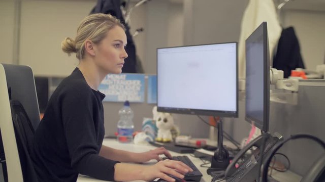 A blonde female employee is working on a computer with two screens.