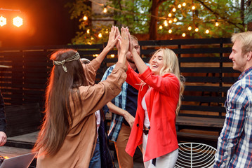 Group of young caucasian friends giving high five together and celebrating party in house courtyard...