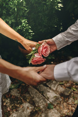 Newlyweds with their hands clasped. Selective focus on bouquet os roses. Union and love concept.