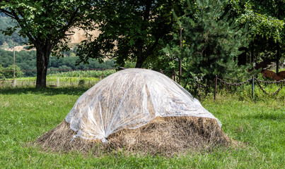 Old-fashioned hay stack covered in plastic in field with heavy chain fence around it and shale mine through the trees in the Georgian Countryside in Eurasia © Susan Vineyard 