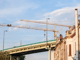 Peri urban scenery of the suburb of Belgrade, with cranes on a construction site behind old houses soon to be destroyed and an old concrete road bridge, in an area being redeveloped