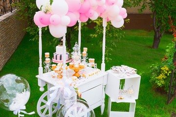 Candy Bar. White wooden trolley with sweets decorated with balloons on green grass
