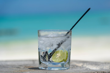 Soda water with lime and ice on a wooden table near the sea on the beach