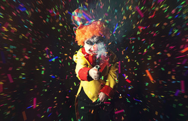 Evil scary clown explodes a party Popper standing on a black background.  Party with confetti and...