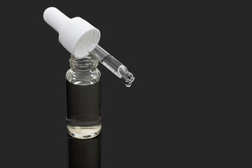 Bottle and a dropper with a moisturizing serum against a dark background close up copy space