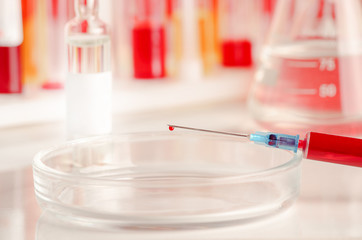 Syringe with a blood sample on the background of medical ampoules and laboratory glassware. Virus epidemic, medical concept.