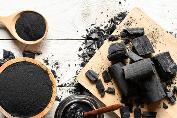 Black charcoal powder for facial mask and scrub, placed on a white wooden table, health and beauty concept.